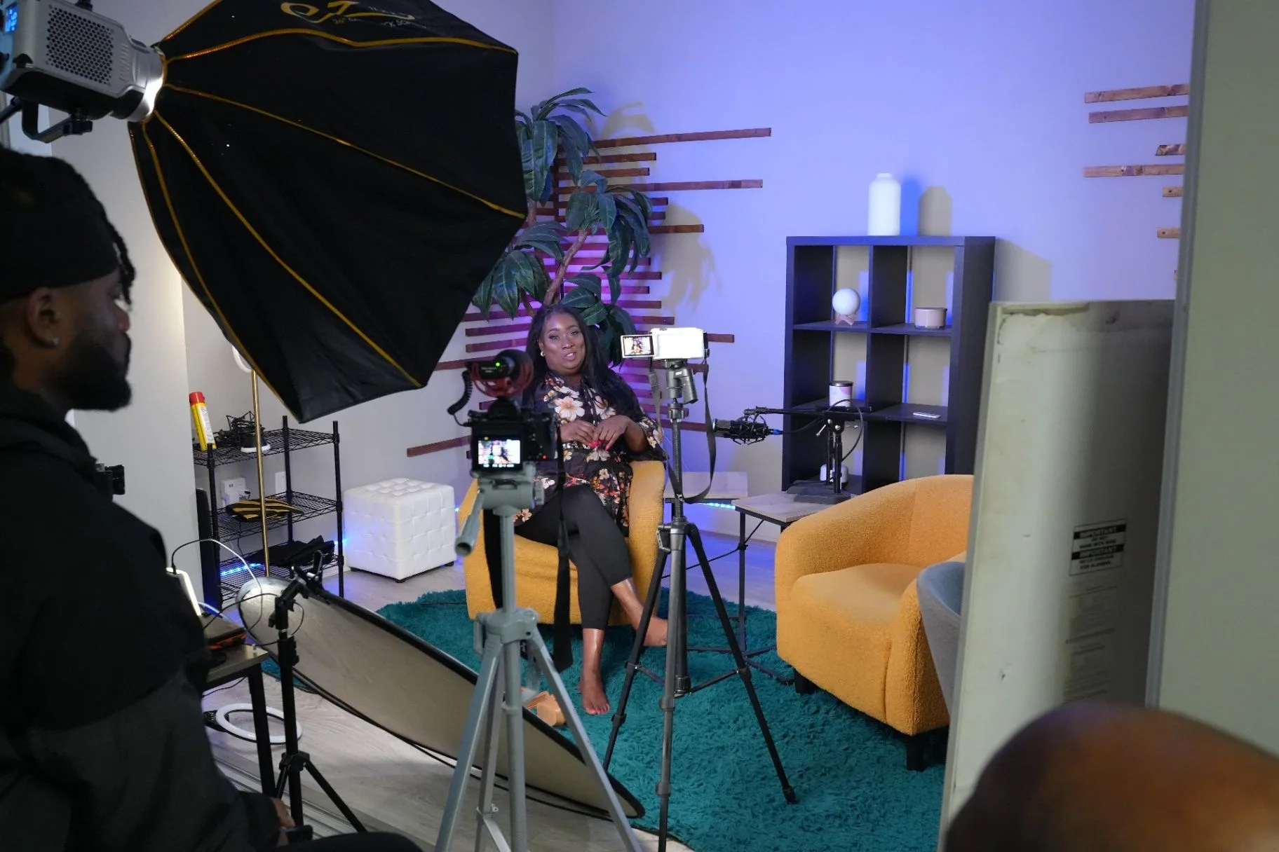 Podcast studio setup with a camera, softbox lights, microphones, and a seated guest ready to record.